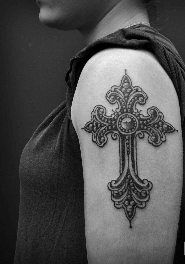 A foto da tatuagem de uma cruz em estilo gótico no ombro da menina