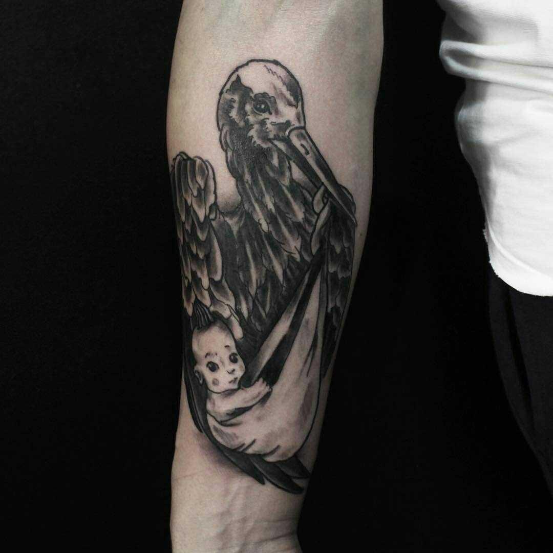 A tatuagem da cegonha com o bebê no antebraço cara