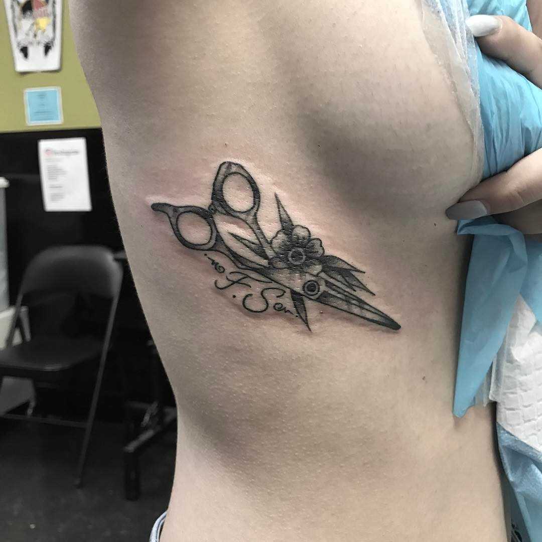 A tatuagem da tesoura com a flor no lado da menina