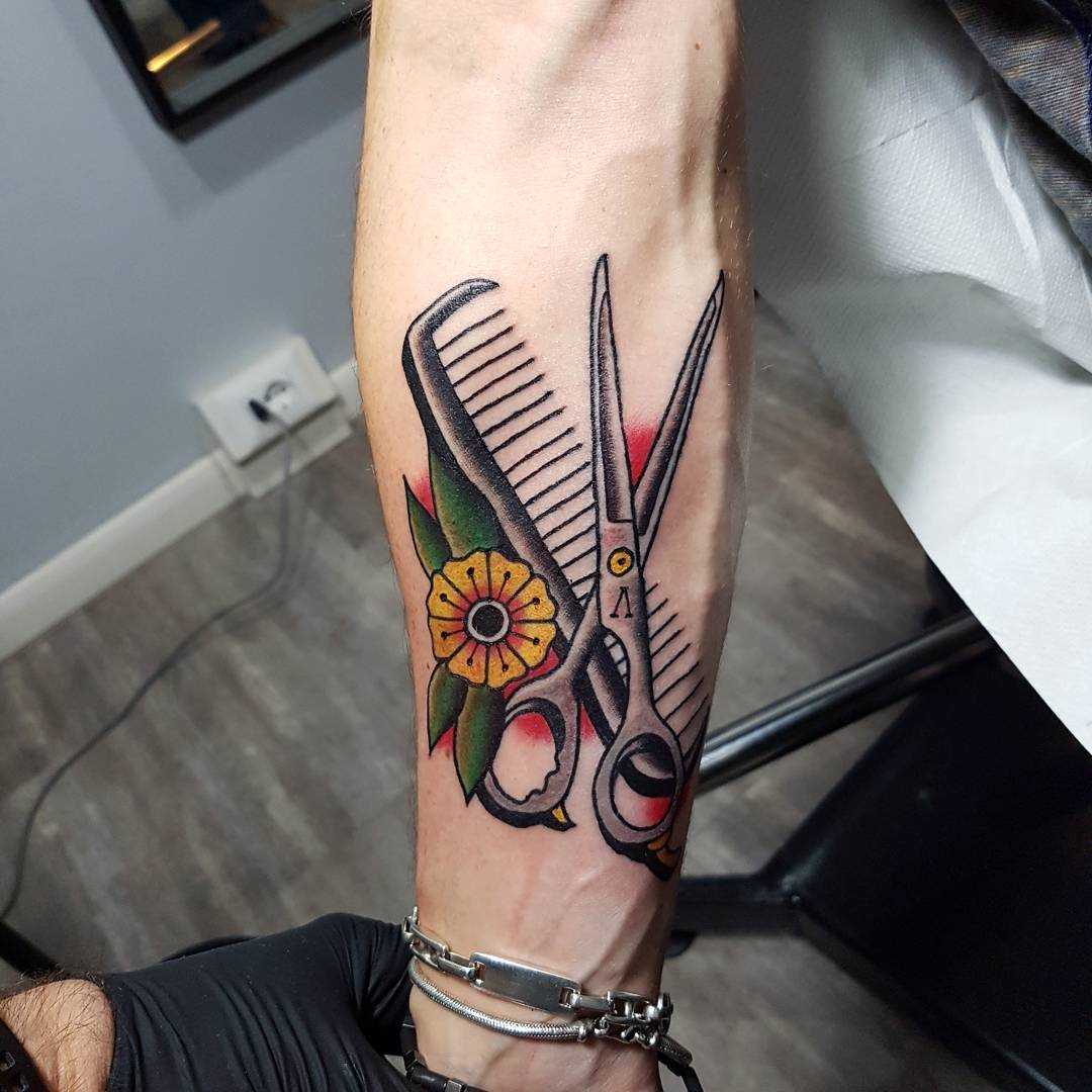 A tatuagem da tesoura com um pente no antebraço cara