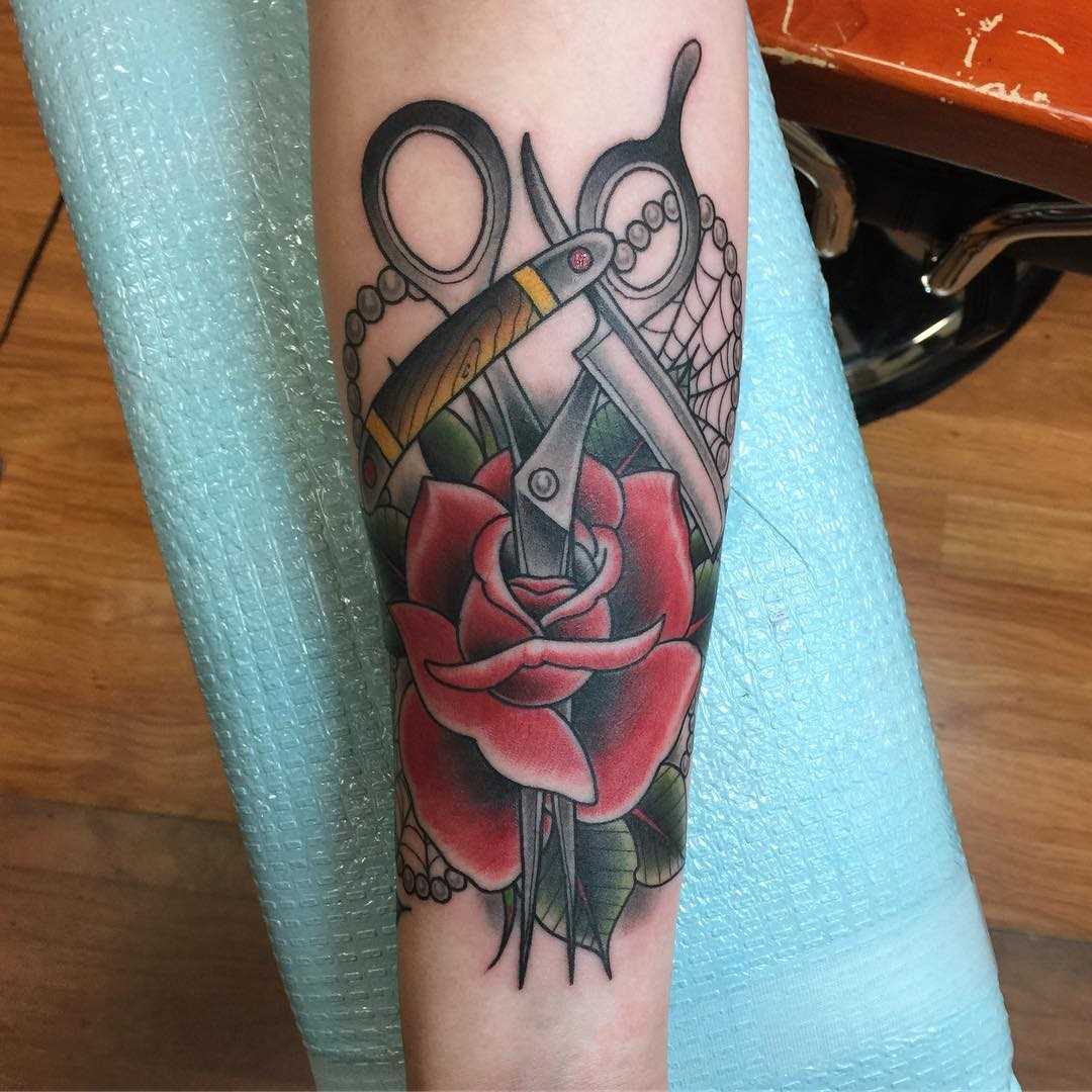 A tatuagem da tesoura com uma rosa no antebraço da menina
