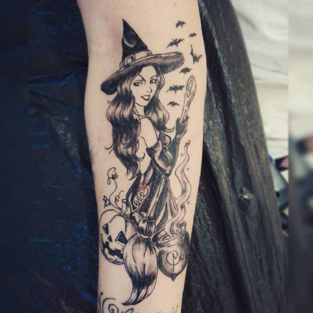 A tatuagem de bruxa com uma vassoura no antebraço da menina