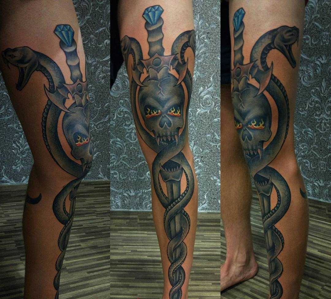 A tatuagem de uma espada com cobras e o crânio na perna do cara