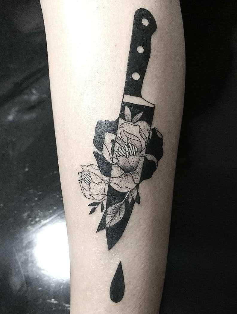 A tatuagem de uma faca com flores sobre a perna da mulher