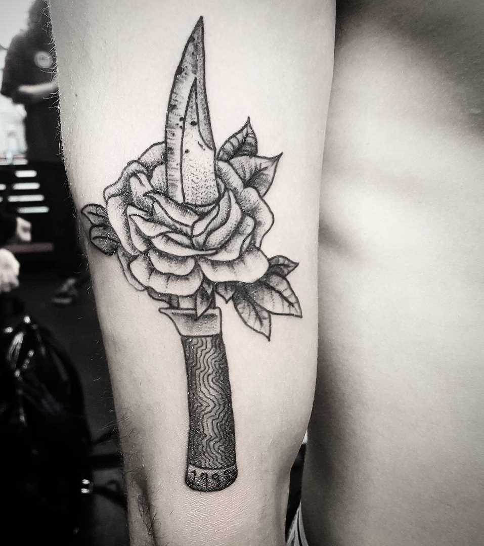 A tatuagem de uma faca com uma rosa na mão do cara