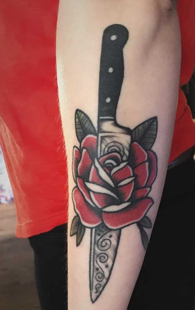 A tatuagem de uma faca com uma rosa no antebraço cara