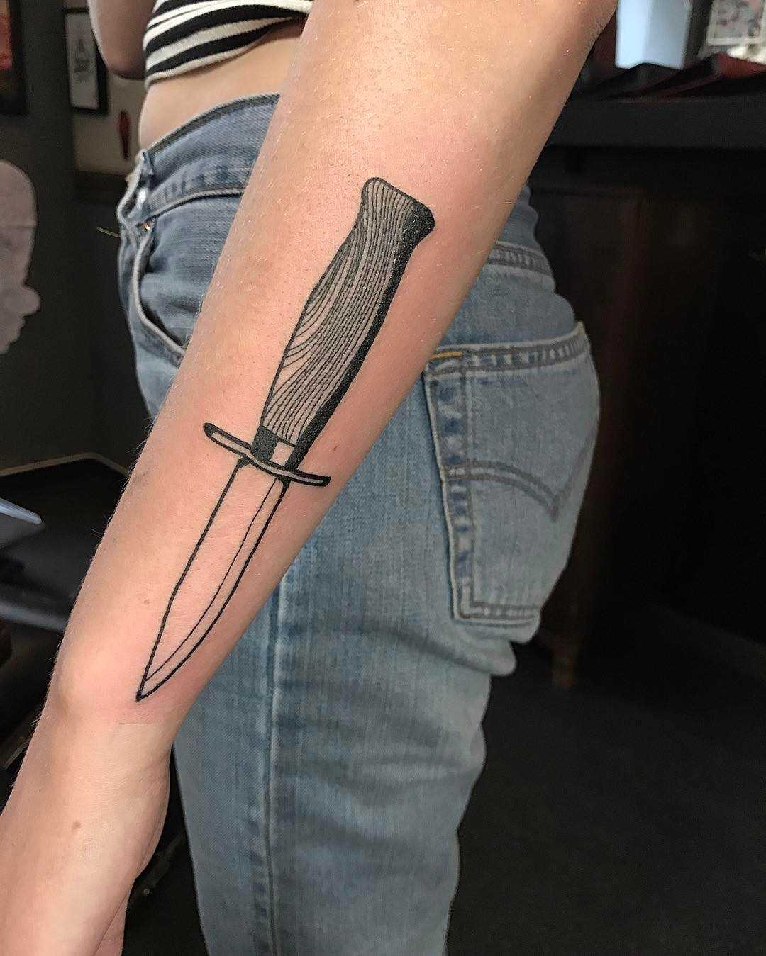 A tatuagem de uma faca sobre o antebraço menina