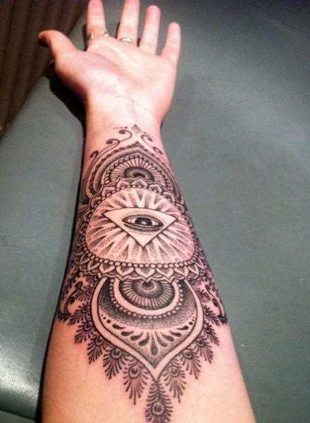 A tatuagem de uma menina no antebraço - mandala e o olho no triângulo,