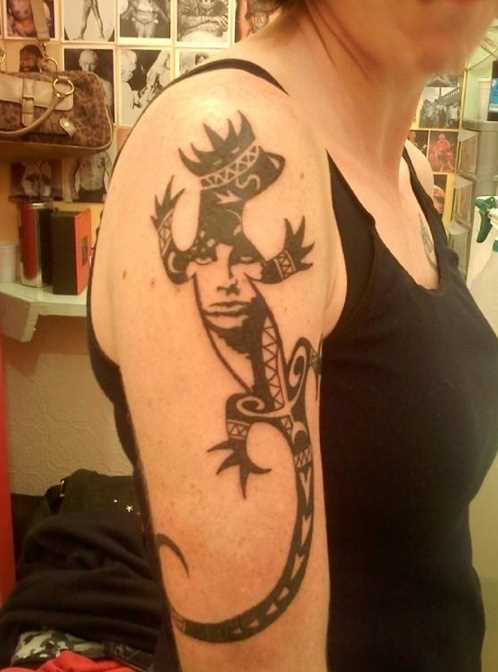 A tatuagem de uma menina no ombro - lagarto com a coroa na cabeça