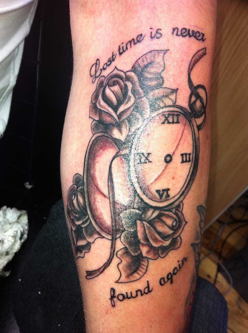 A tatuagem do cara no antebraço - relógio de bolso, rosas e legenda em inglês