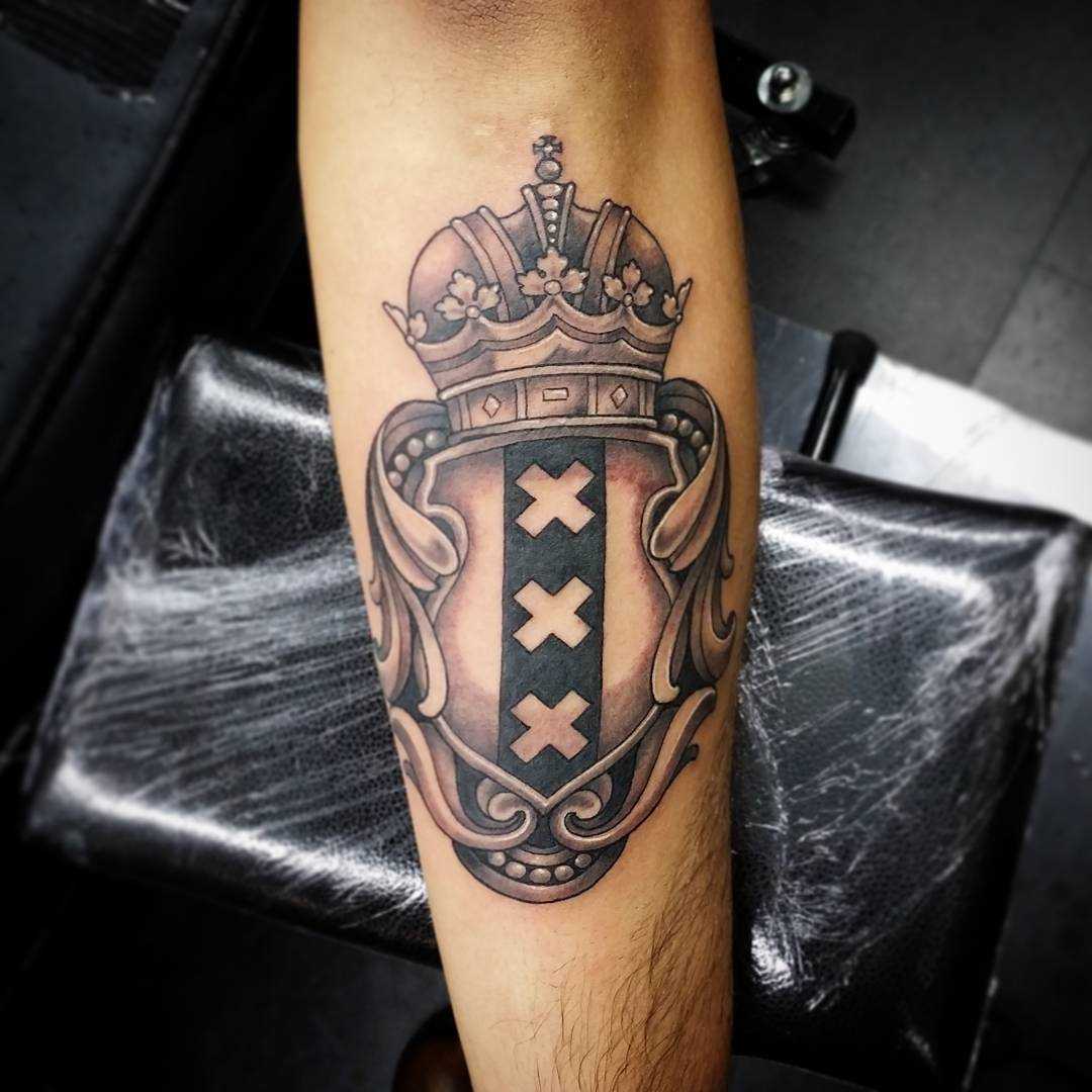 A tatuagem do escudo com a coroa no antebraço cara