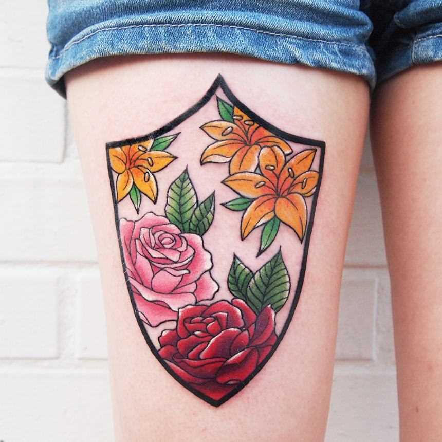 A tatuagem do escudo com as rosas e a coxa da menina
