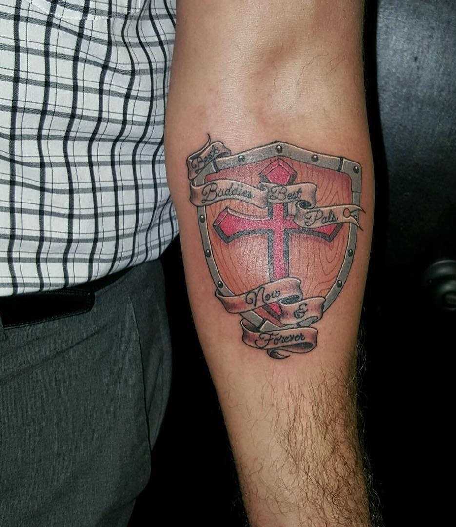 A tatuagem do escudo com uma cruz no antebraço homens