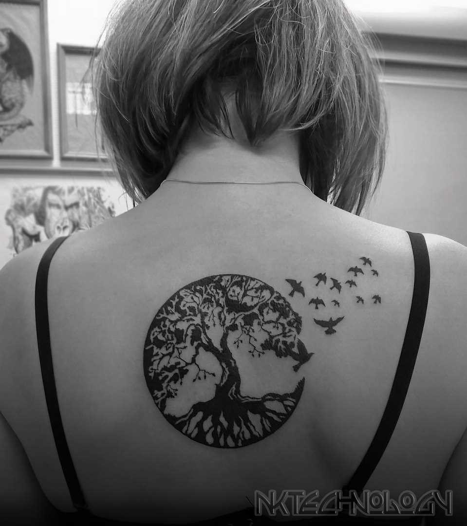 A tatuagem nas costas de uma menina - árvore e passarinhos