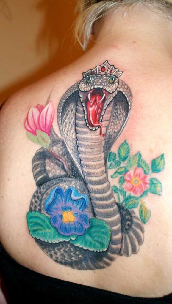 A tatuagem nas costas de uma menina de cobra e de flores