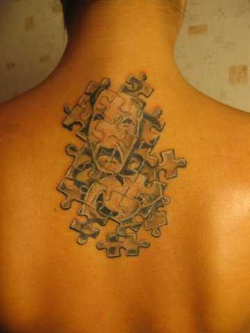 A tatuagem nas costas de uma menina de quebra - cabeça na forma de máscaras