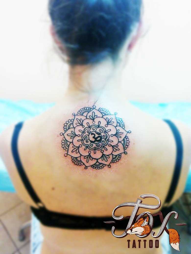 A tatuagem nas costas de uma menina - mandala e o símbolo Ohm
