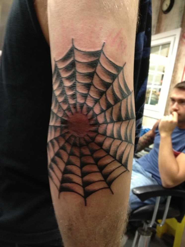 A tatuagem no cotovelo de um cara em uma teia de