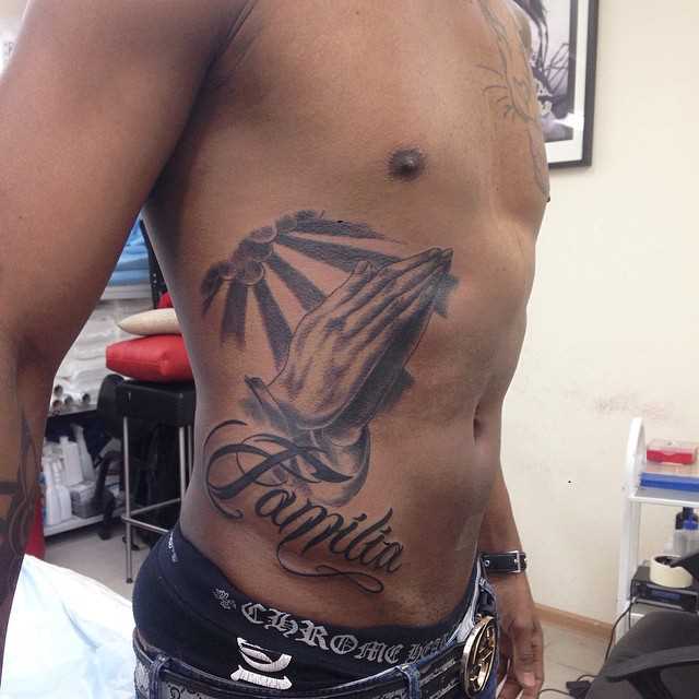A tatuagem no estilo chicano ao lado de um cara - de mãos em oração