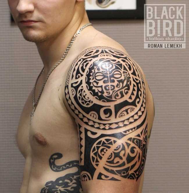 A tatuagem no estilo tribal no ombro de um cara - maiianskaia máscara