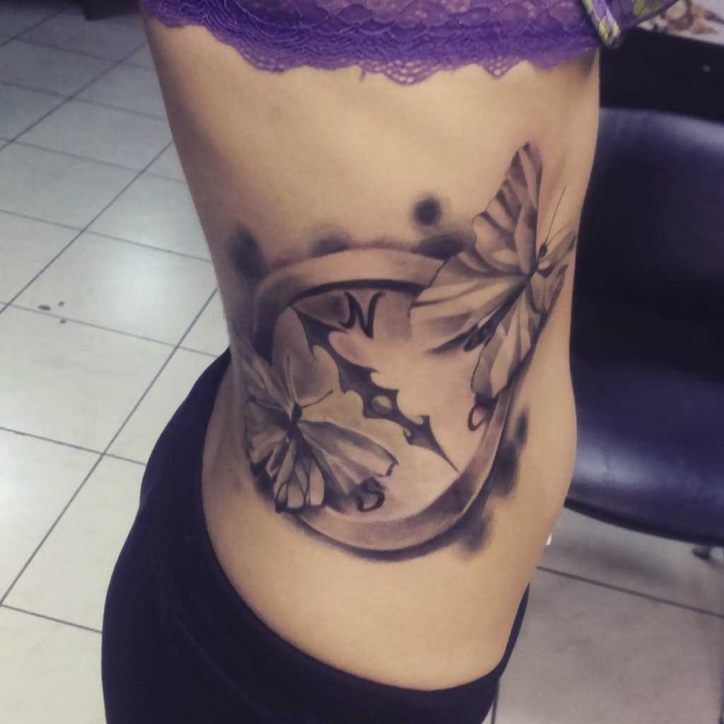 A tatuagem no lado da menina - borboleta e bússola