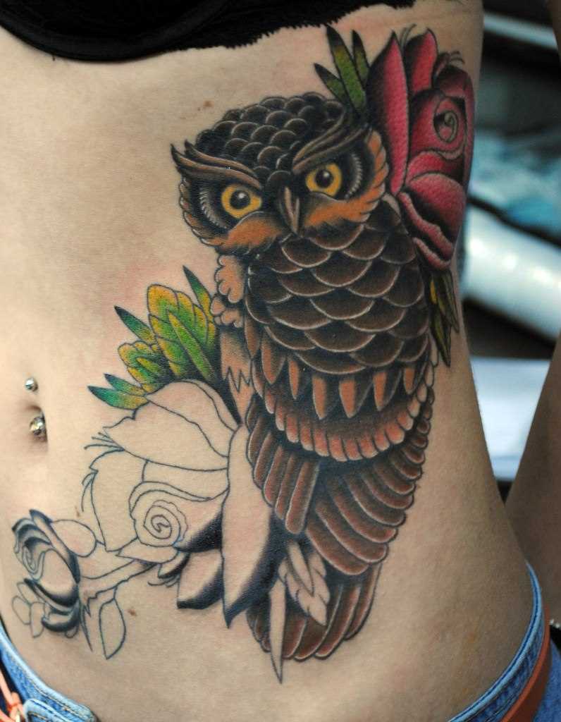 A tatuagem no lado da menina - coruja e flores