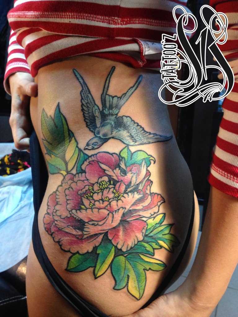 A tatuagem no lado da menina - flor e a andorinha