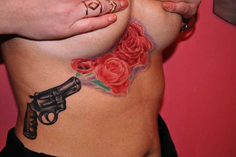 A tatuagem no lado da menina - um revólver e rosas