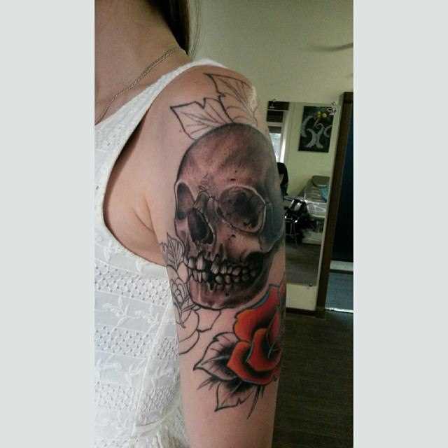 A tatuagem no ombro da menina de crânio e rosas