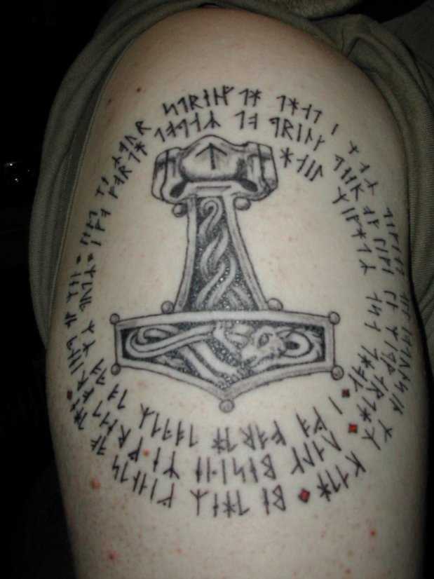 A tatuagem no ombro de um cara com a imagem de um martelo e inscrições