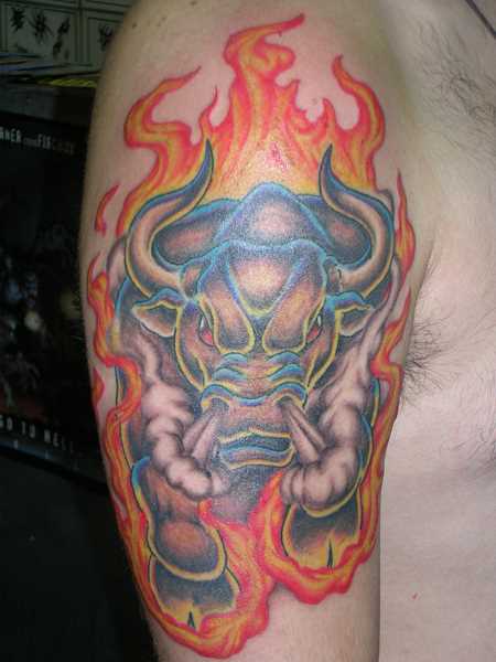 A tatuagem no ombro de um cara com a imagem de um touro e fogo