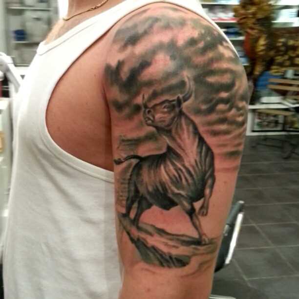 A tatuagem no ombro de um cara com a imagem de um touro sobre a rocha