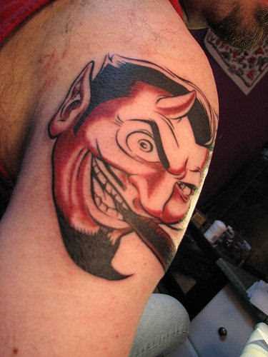 A tatuagem no ombro de um cara com a imagem do diabo com o cigarro