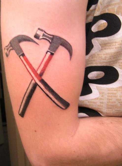 A tatuagem no ombro de um cara com uma foto de dois martelos
