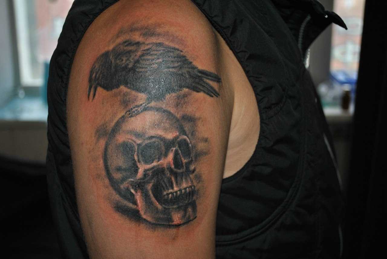 A tatuagem no ombro de um cara de crânio e o corvo