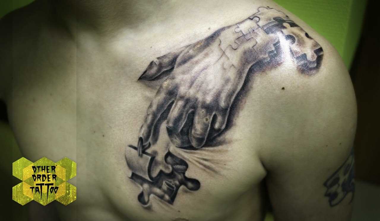 A tatuagem no ombro de um cara de quebra - cabeça e a mão de