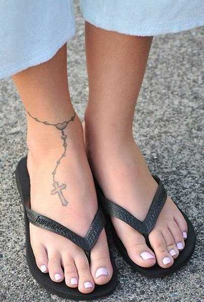 A tatuagem no tornozelo preto da menina - um colar com uma cruz