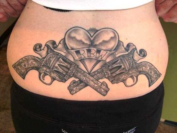 A tatuagem tinta preta no estilo oldschool na lombar menina pistolas e coração