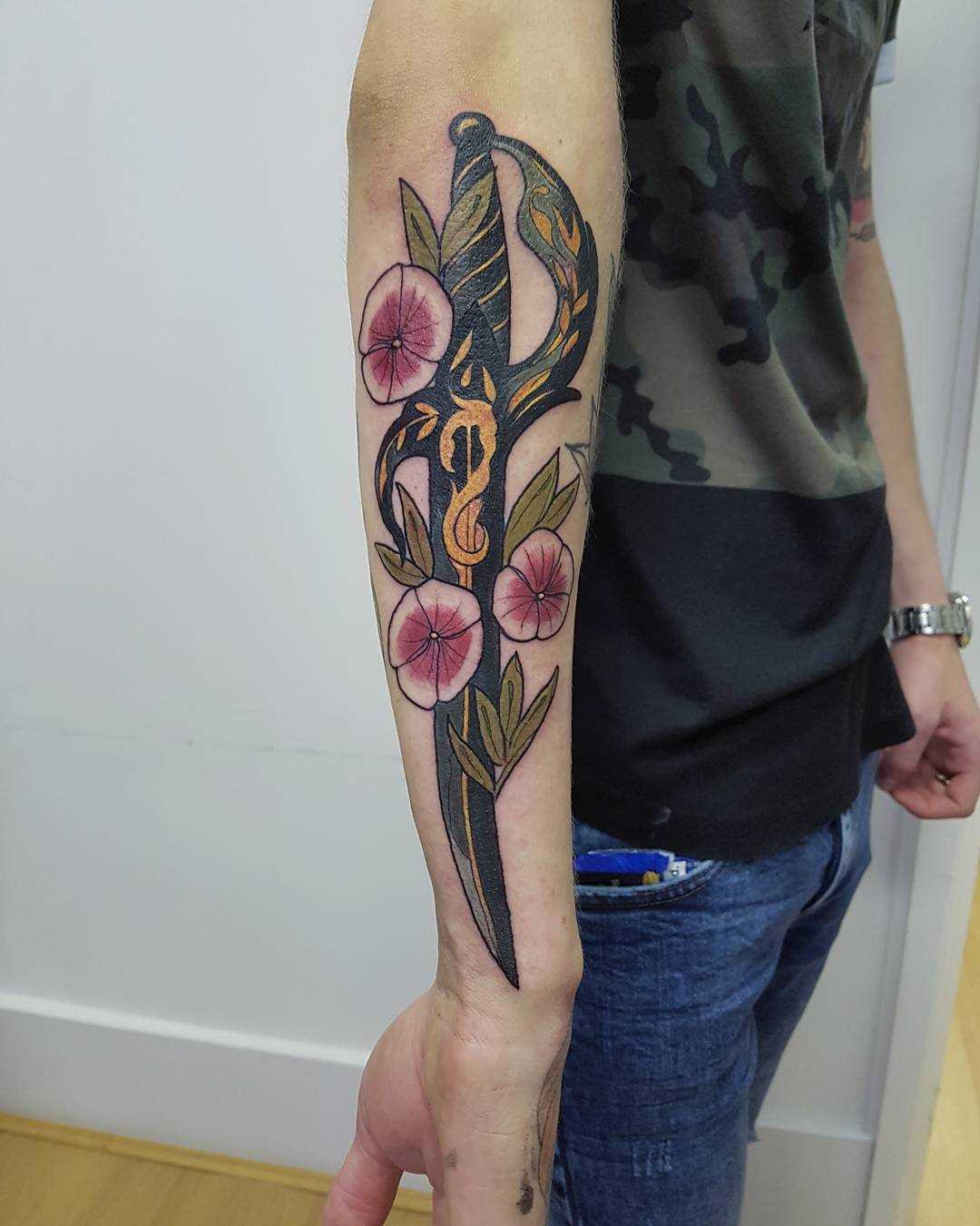 Bela tatuagem adaga com flores no antebraço cara