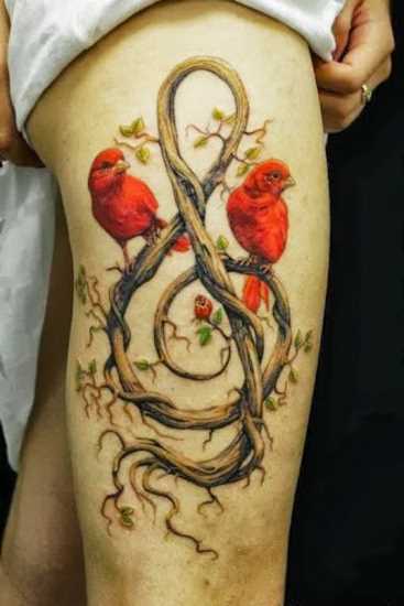 Bela tatuagem nas coxas da menina - clave de sol em forma de galhos de árvores e os pássaros vermelhos