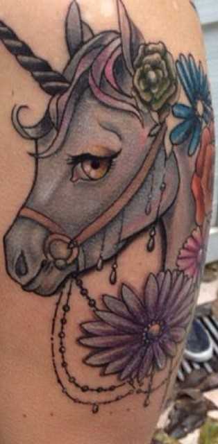 Bela tatuagem no ombro da menina - um unicórnio e flores
