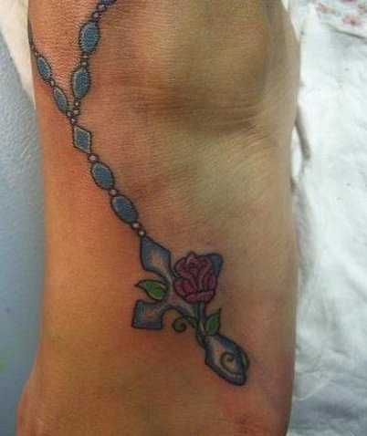 Bela tatuagem no tornozelo preto da menina - um colar com uma cruz e aa