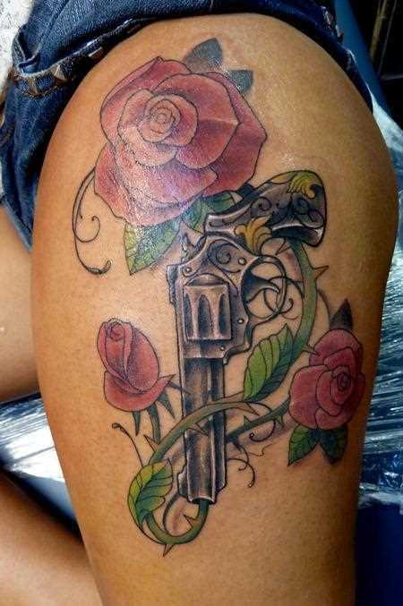 Bela tatuagem que a menina nos quadris em forma de pistola e de rosas