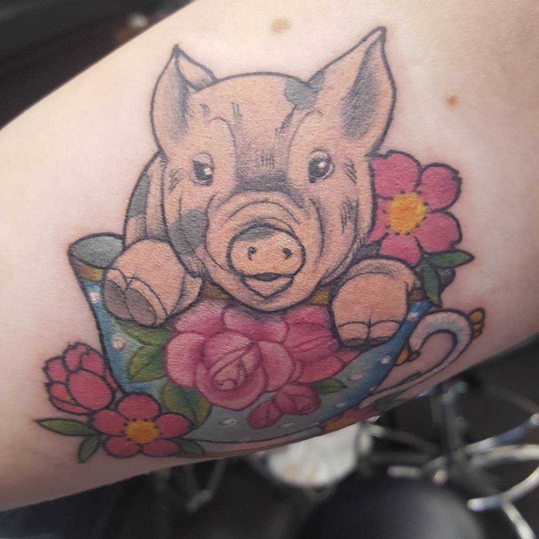 Cores de tatuagem de um porco em um copo sobre a perna da menina