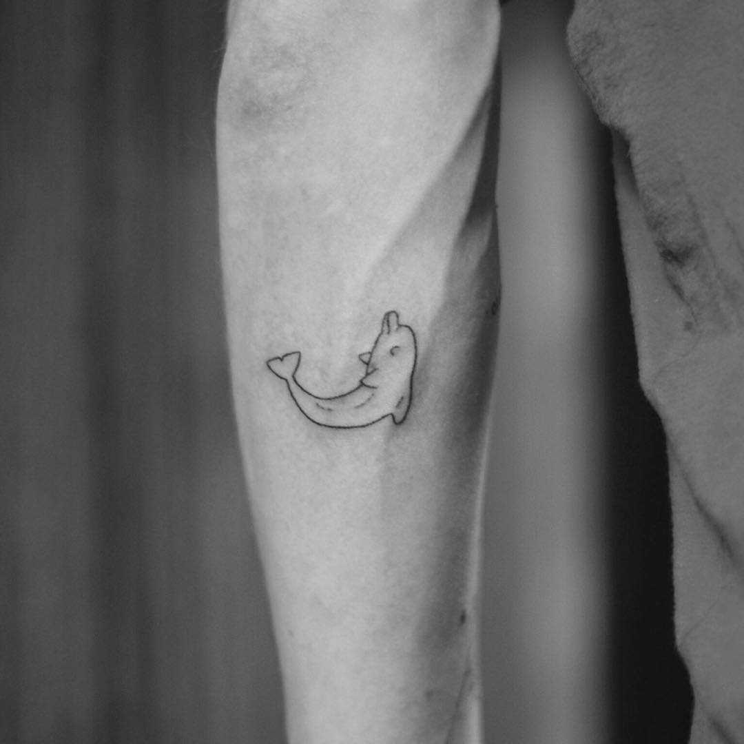 Foto de uma pequena tatuagem de golfinho no estilo handpoke no antebraço cara
