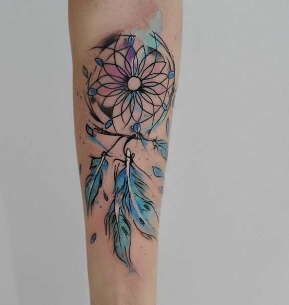 Foto de uma tatuagem de apanhador de sonhos em estilo de aquarela no antebraço da menina
