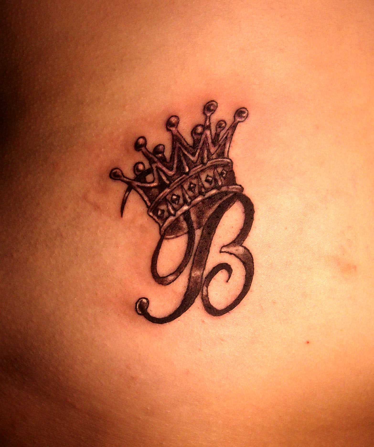 Tatuagem de coroa com a letra A na região lombar, as meninas