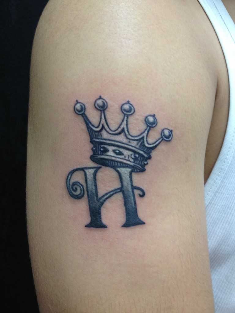 Tatuagem de coroa com a letra E no ombro do cara