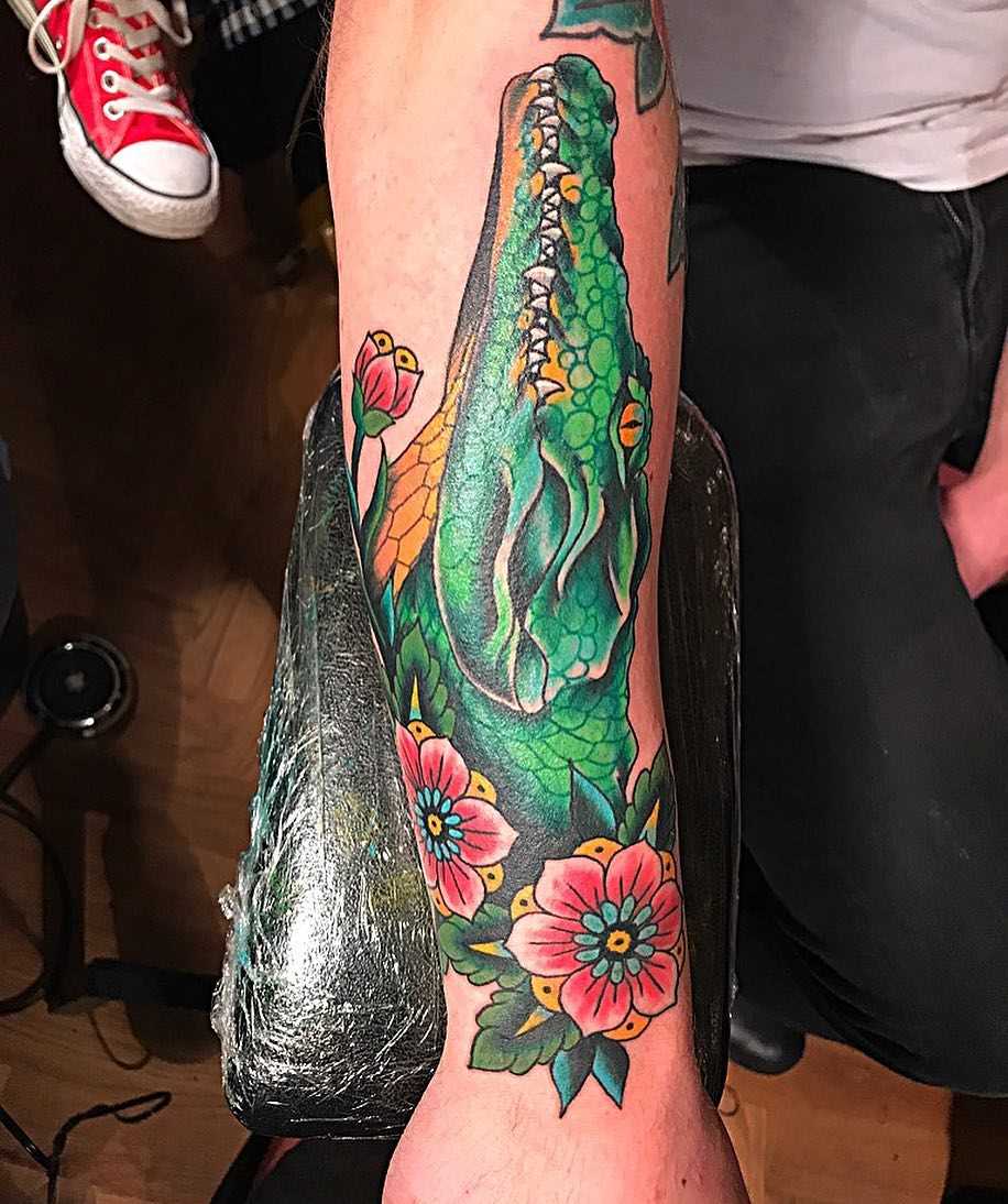 Tatuagem de crocodilo com flores no antebraço cara
