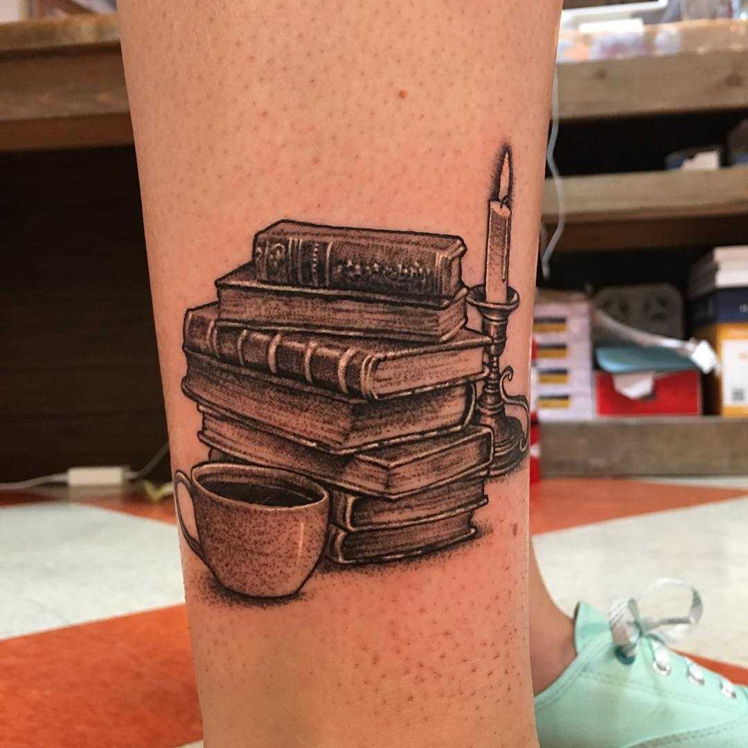 Tatuagem de livros com a caneca sobre a perna da mulher